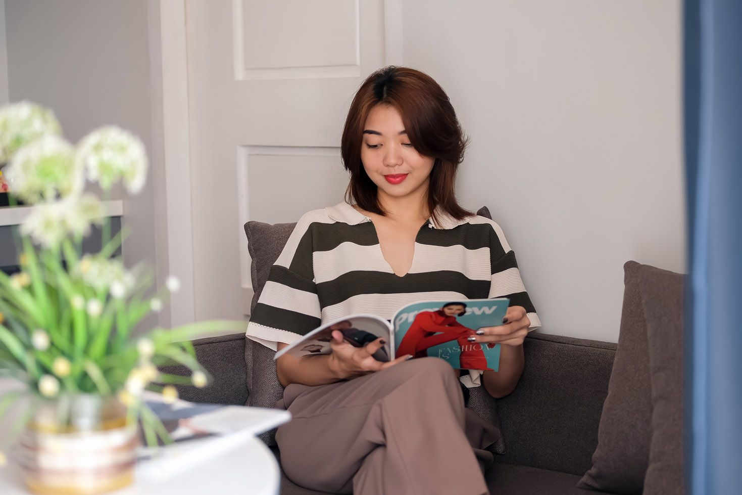 A woman is sitting in a chair reading a magazine.