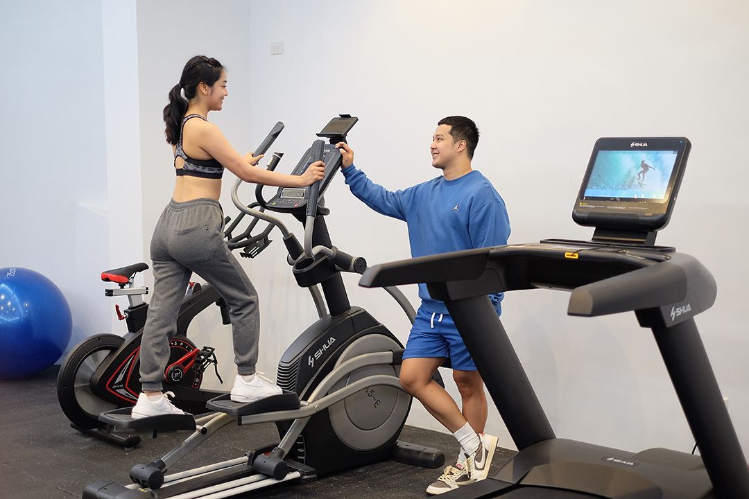 Woman on elliptical, man near treadmill. Both in gym setting, with exercise equipment.