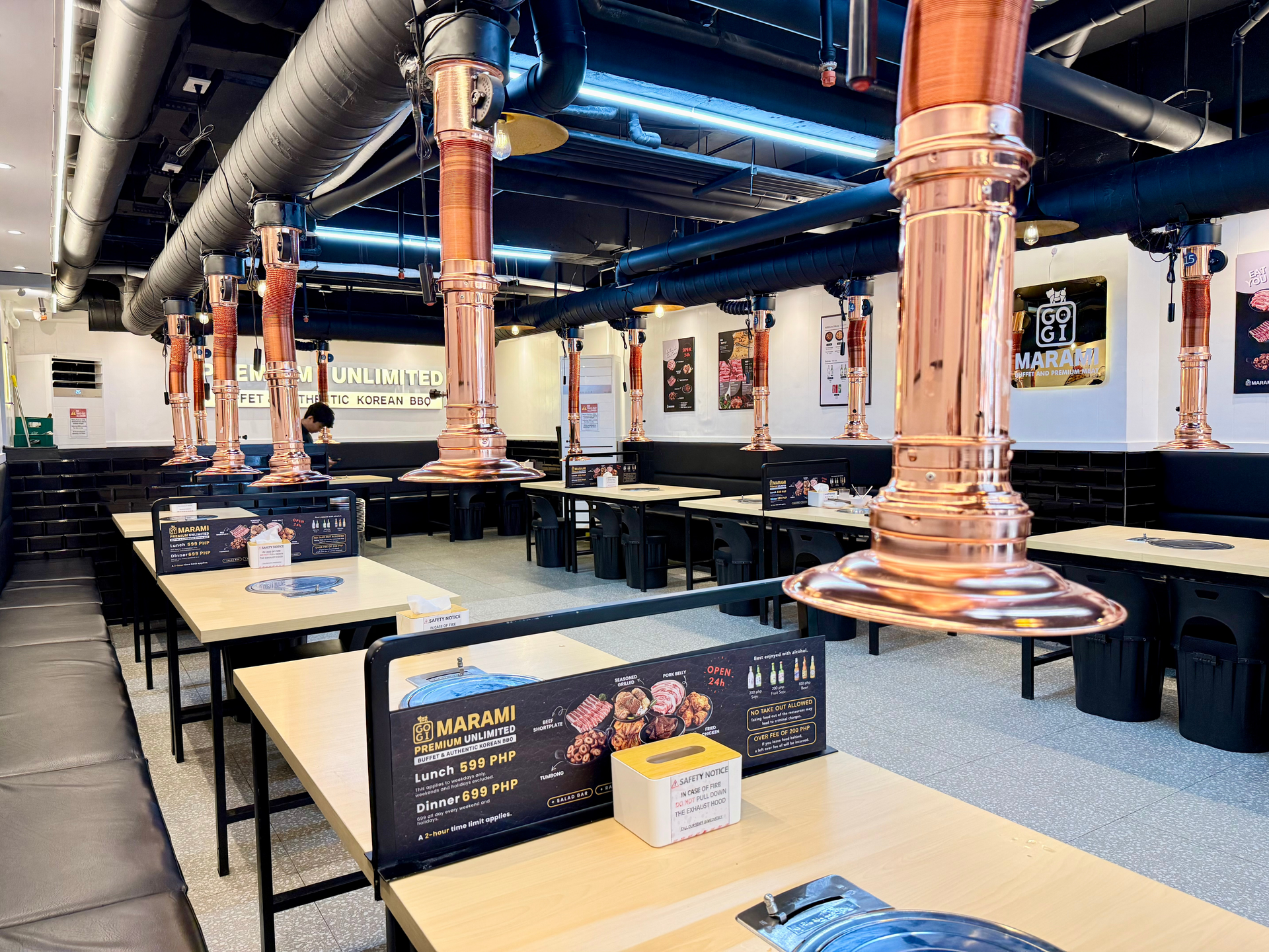 Modern restaurant interior with long tables, black chairs, copper ducts, and wall decor across the room