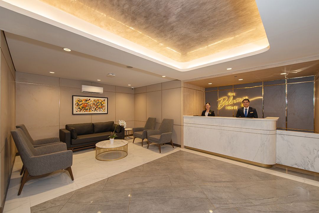 Hotel lobby with a reception desk, staff, seating area, and neutral colors.
