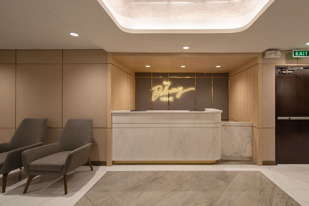 Reception area with a light-colored counter, two chairs, and a neon sign.