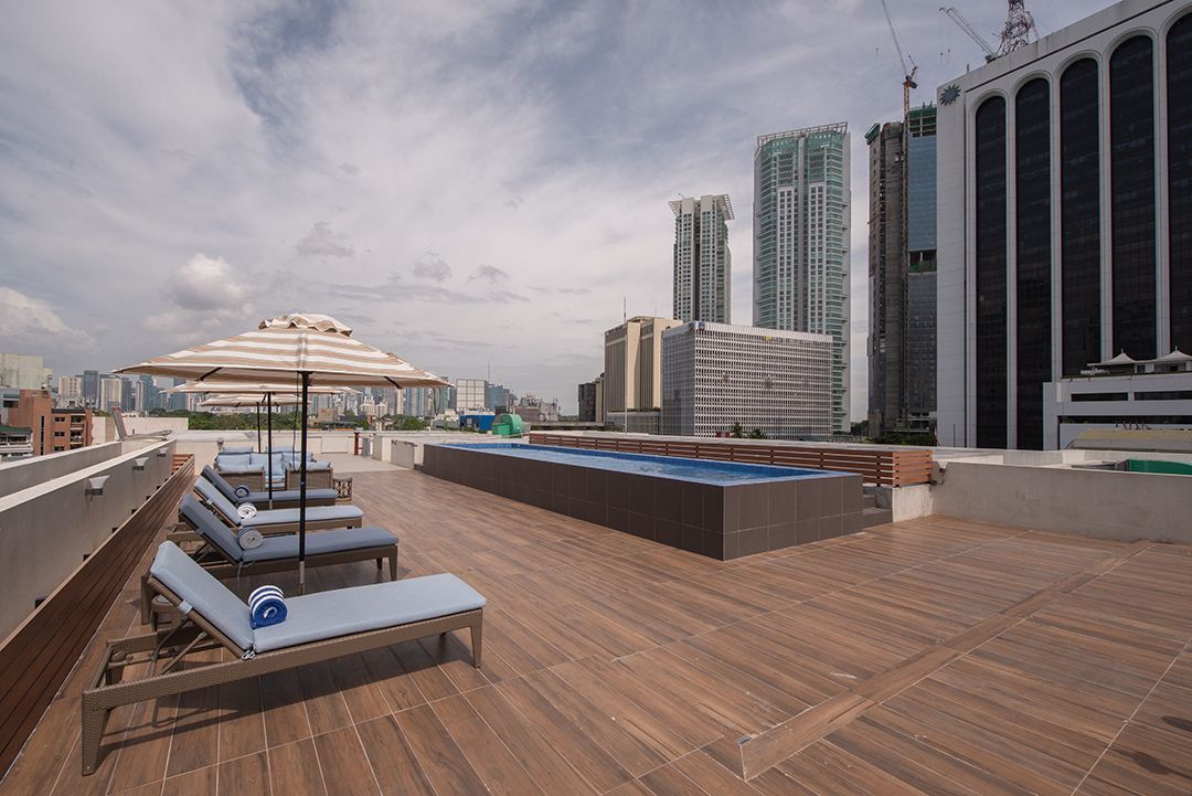 Rooftop pool deck with lounge chairs and umbrella overlooking city skyline.