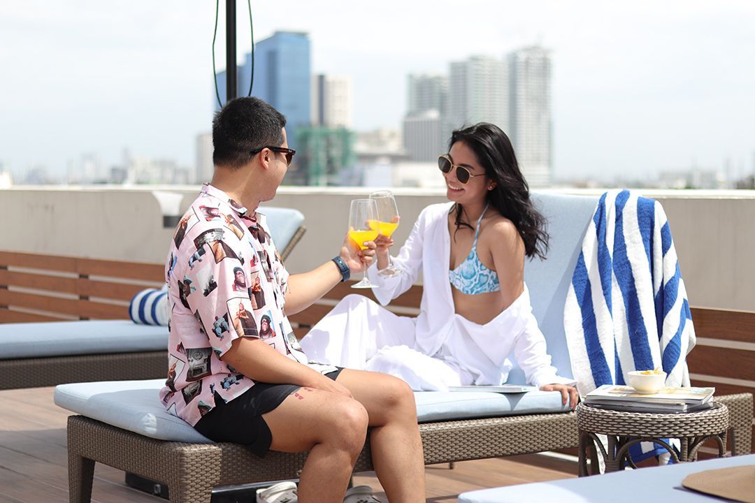 A man and a woman are sitting on lounge chairs with a view of Makati skyline