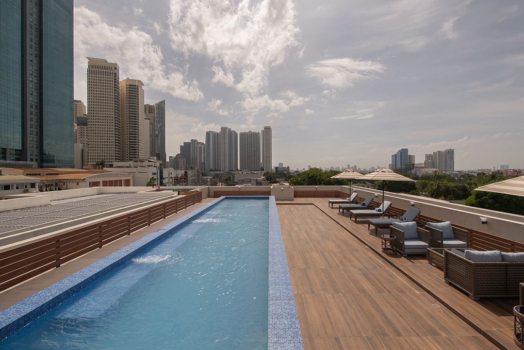 Rooftop pool beside lounge chairs and city skyline under a cloudy sky