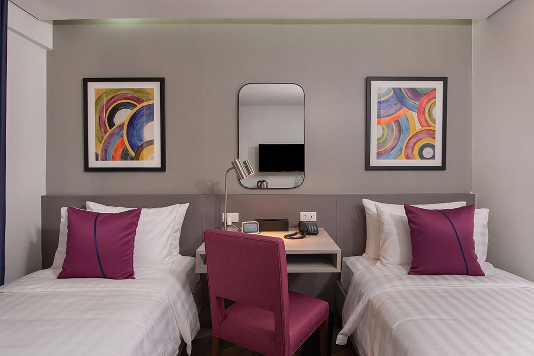 Hotel room with two twin beds, desk, and abstract art on the wall.