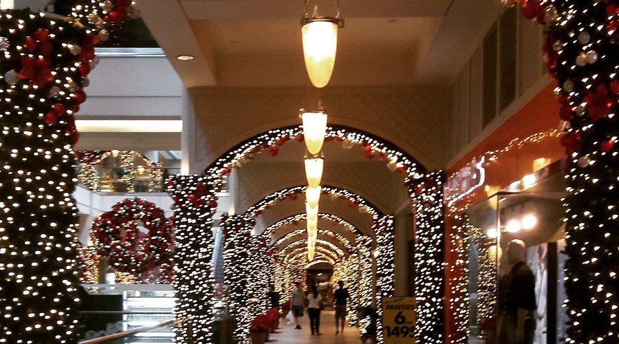 Mall hallway decorated with Christmas lights and garlands, pedestrians walking.