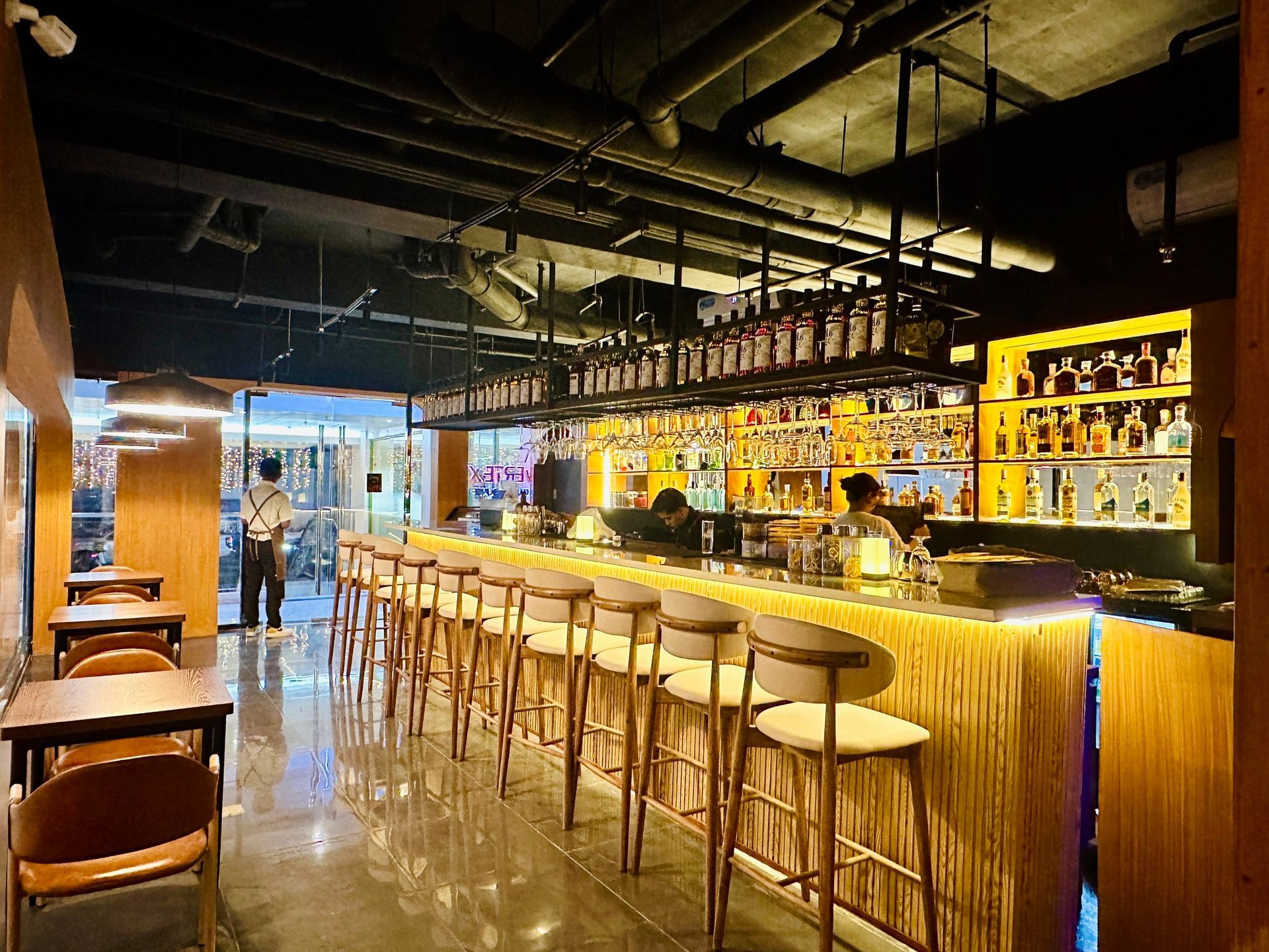 Bar interior with a long counter, stools, and shelves of liquor bottles.