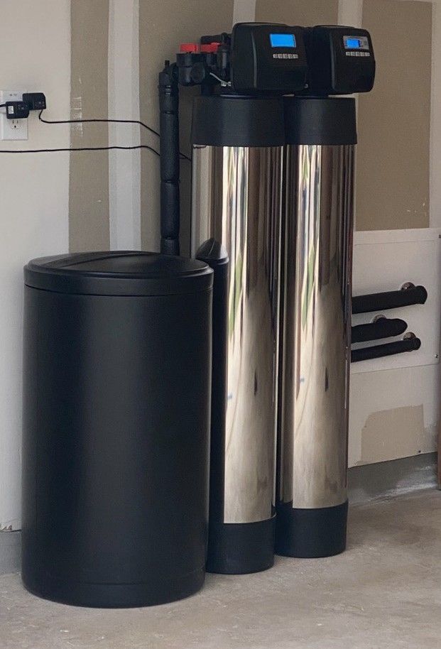 Water softener system: black salt tank, two tall silver tanks with digital displays, garage setting.