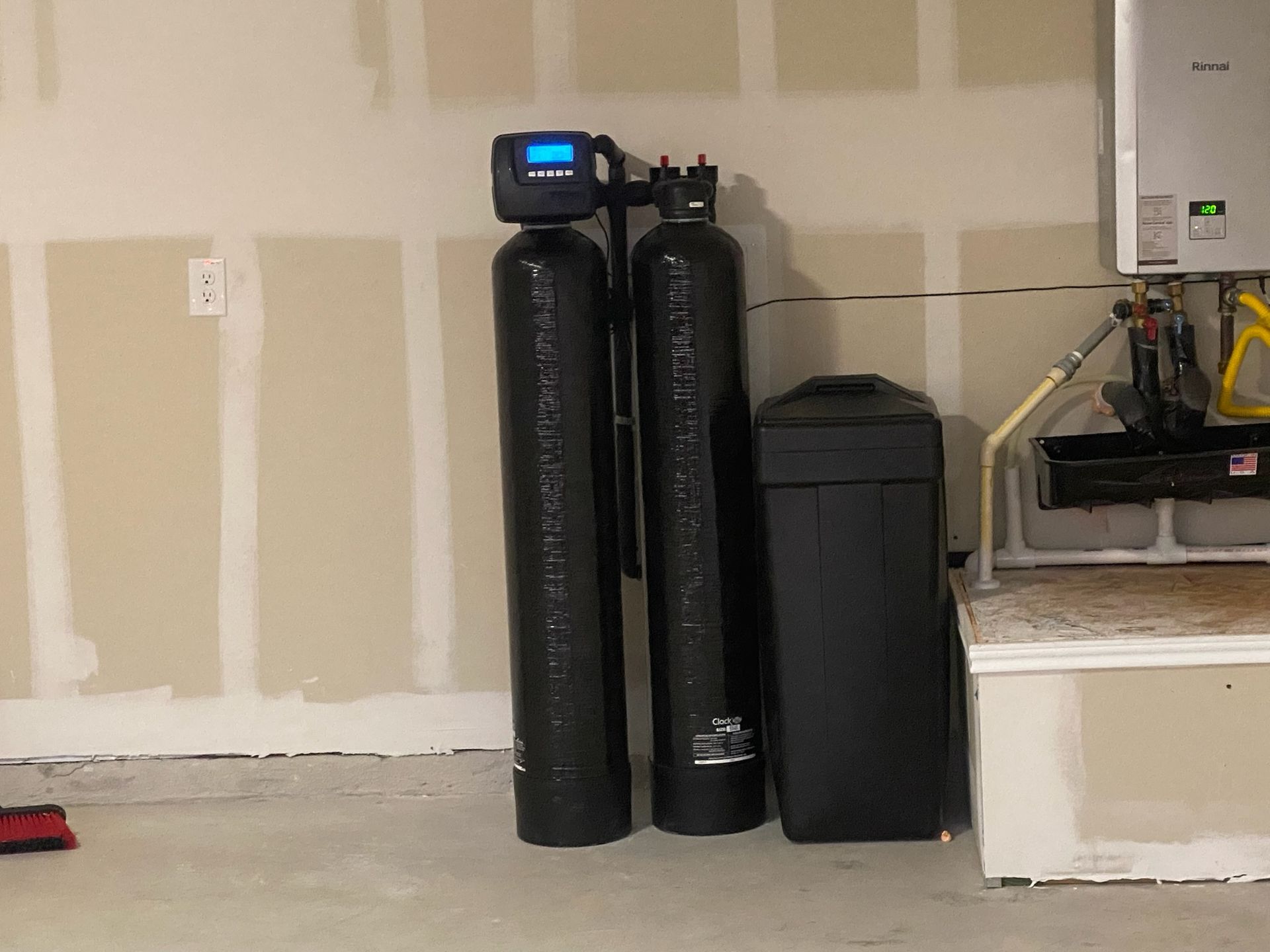 Water filtration system in a garage setting, with tall black tanks and a digital display on one.