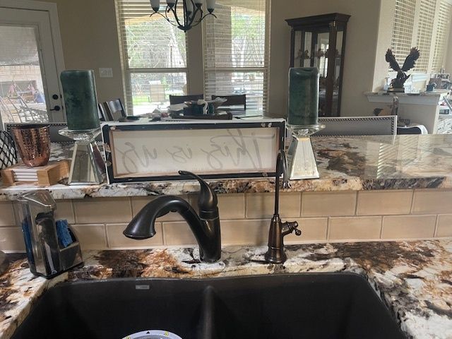 Kitchen sink with dark faucet, granite countertop, and tile backsplash. Two green candles sit on the counter behind the sink.