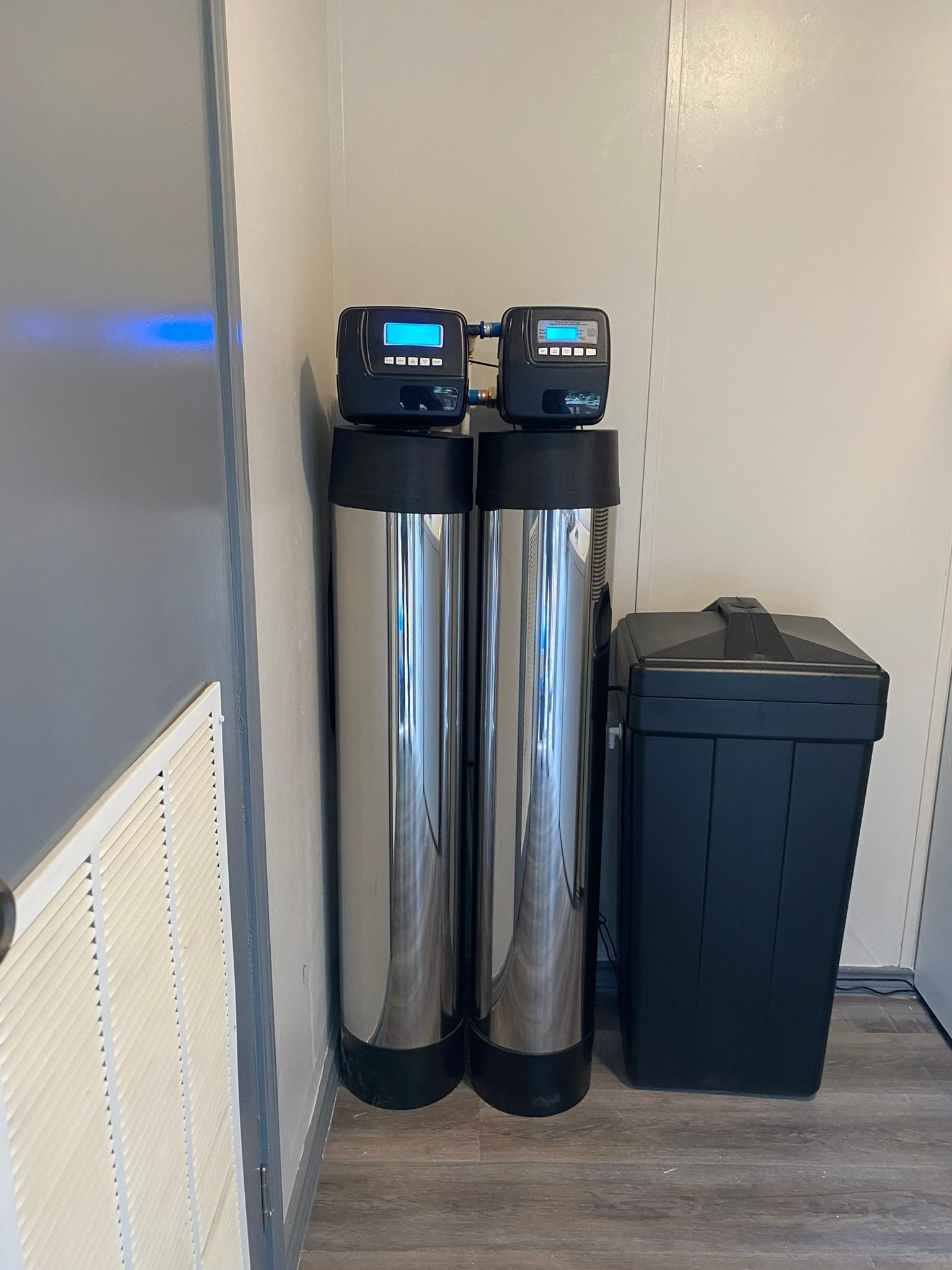 Two silver water filtration tanks with digital displays and a black salt bin, in a corner.