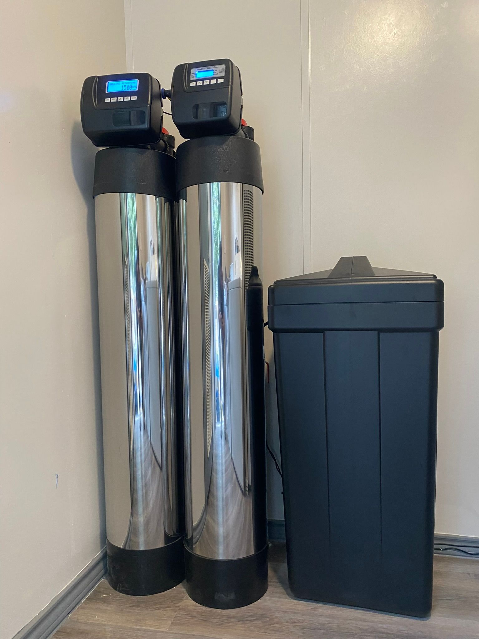 Two tall, silver water filtration tanks with black tops and a black salt storage tank, indoors.