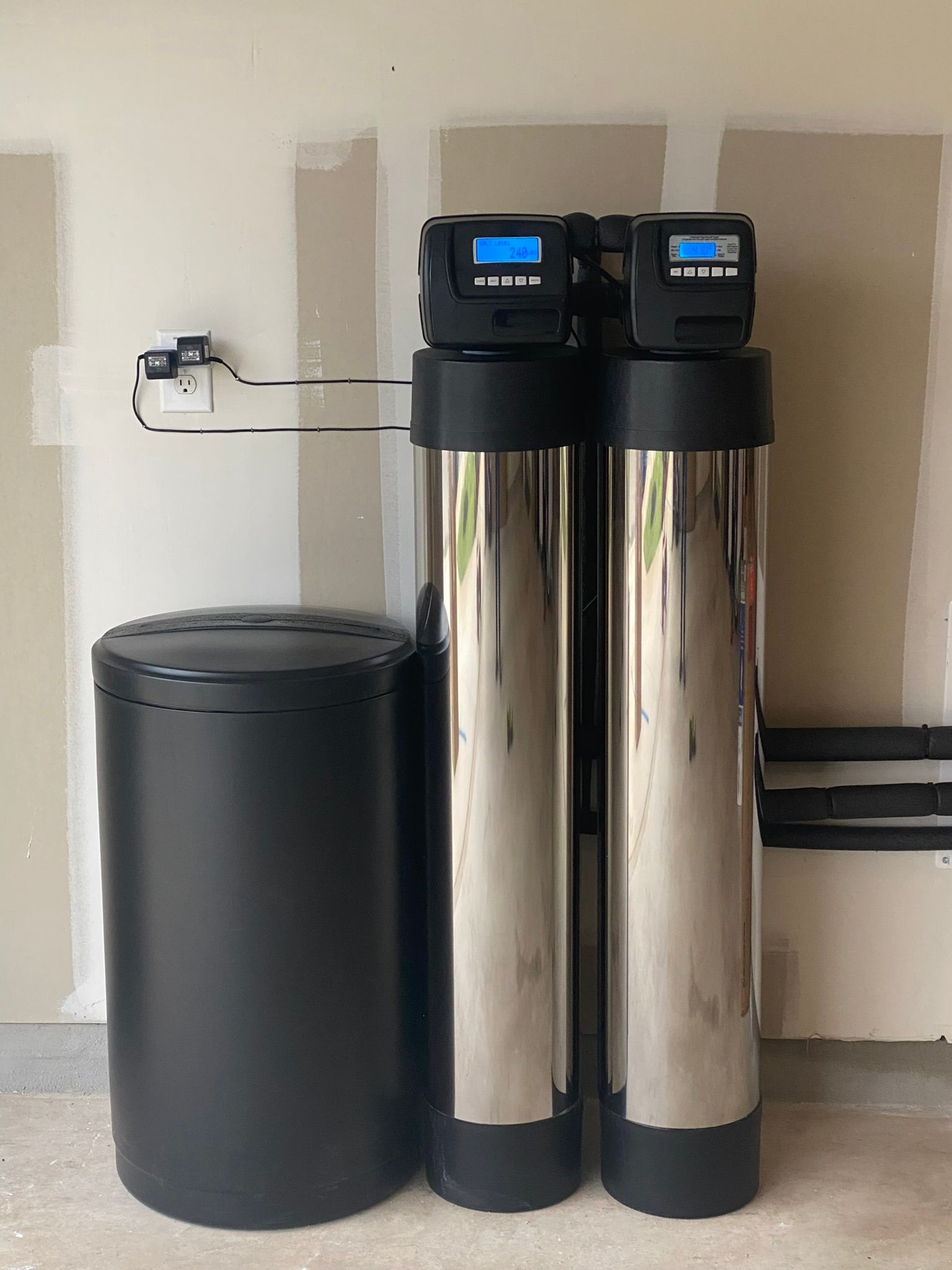 Water softener system with black tank and two chrome tanks, mounted on a wall.