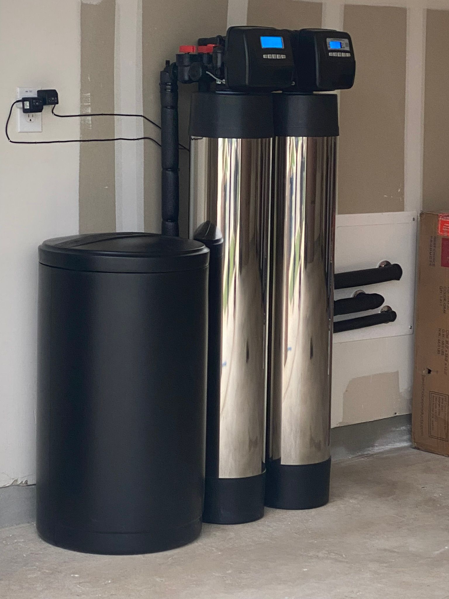 Water filtration system in a garage: black tank, two tall silver tanks, and a control panel.
