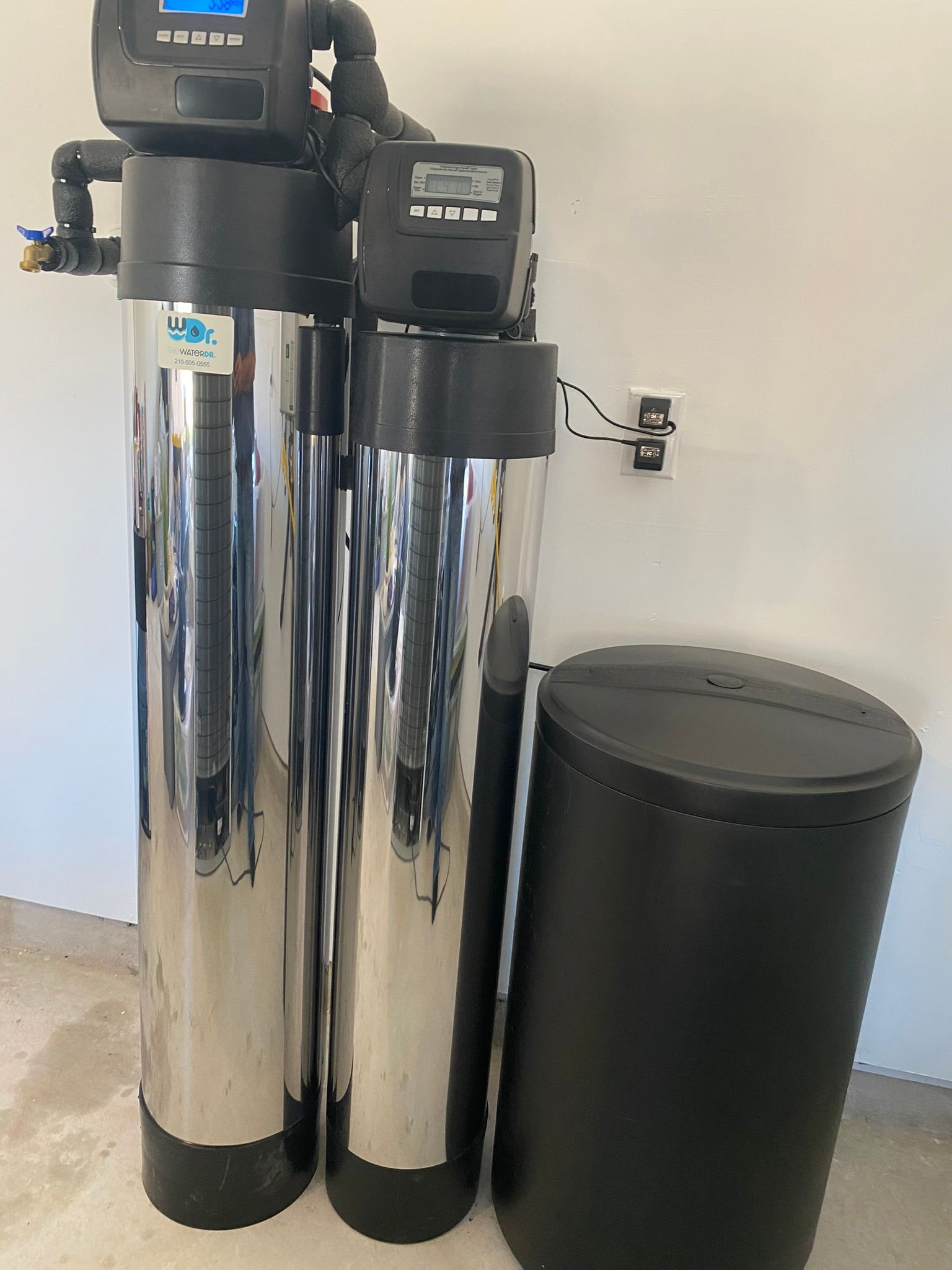 Water softener system with tall, shiny metal tanks, and a black salt tank.