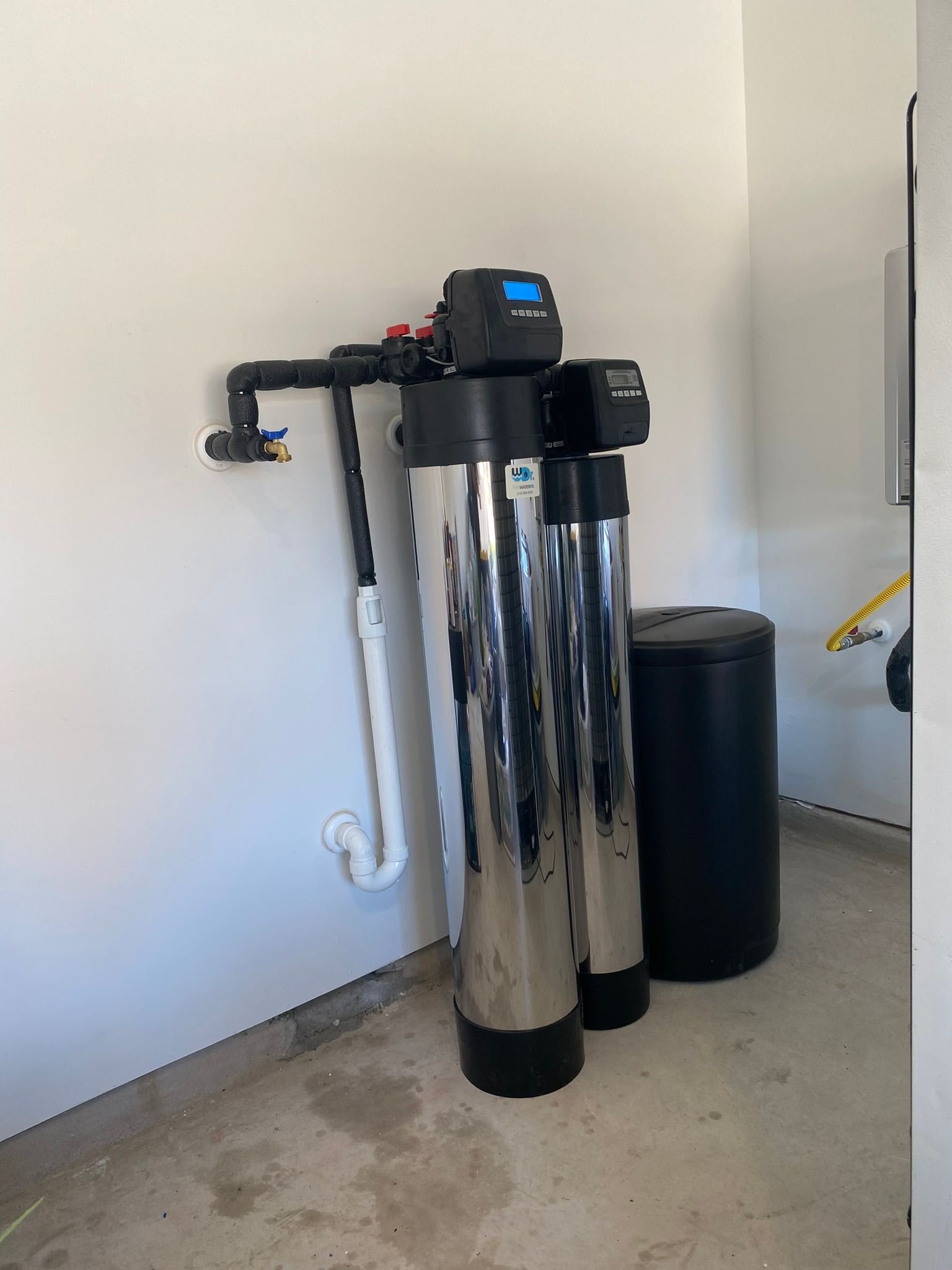 Water filtration system in a garage. Two stainless steel tanks, control unit, and a black brine tank.