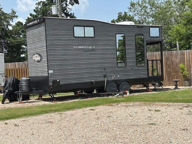 Gray and black modern camper trailer parked on grass and gravel.