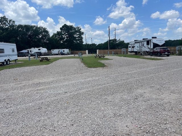 RV park with gravel parking, picnic tables, and recreational vehicles under a cloudy sky.