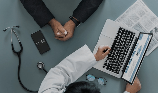 A doctor is using a laptop computer while talking to a patient.