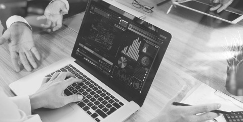 Black and white image of two people discussing on the table with a laptop showing charts.