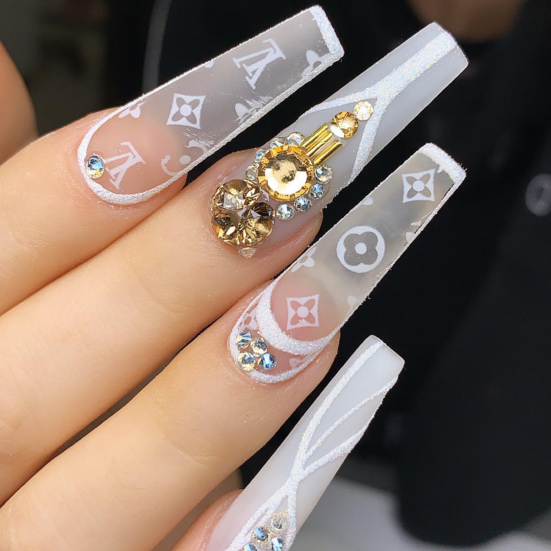 A close up of a woman 's nails with a louis vuitton design and rhinestones.