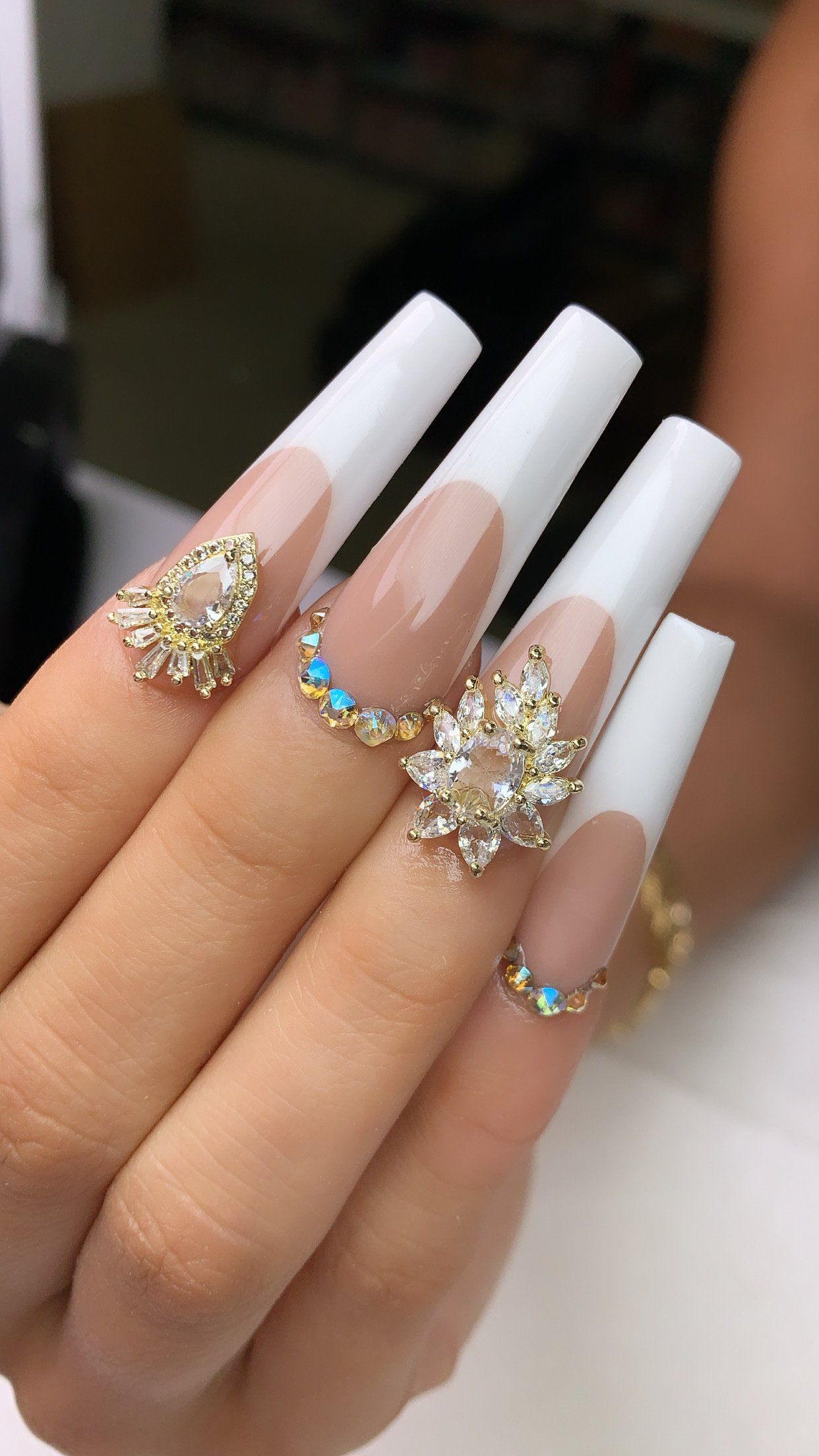 A woman 's hand with long white nails and rhinestones on them.