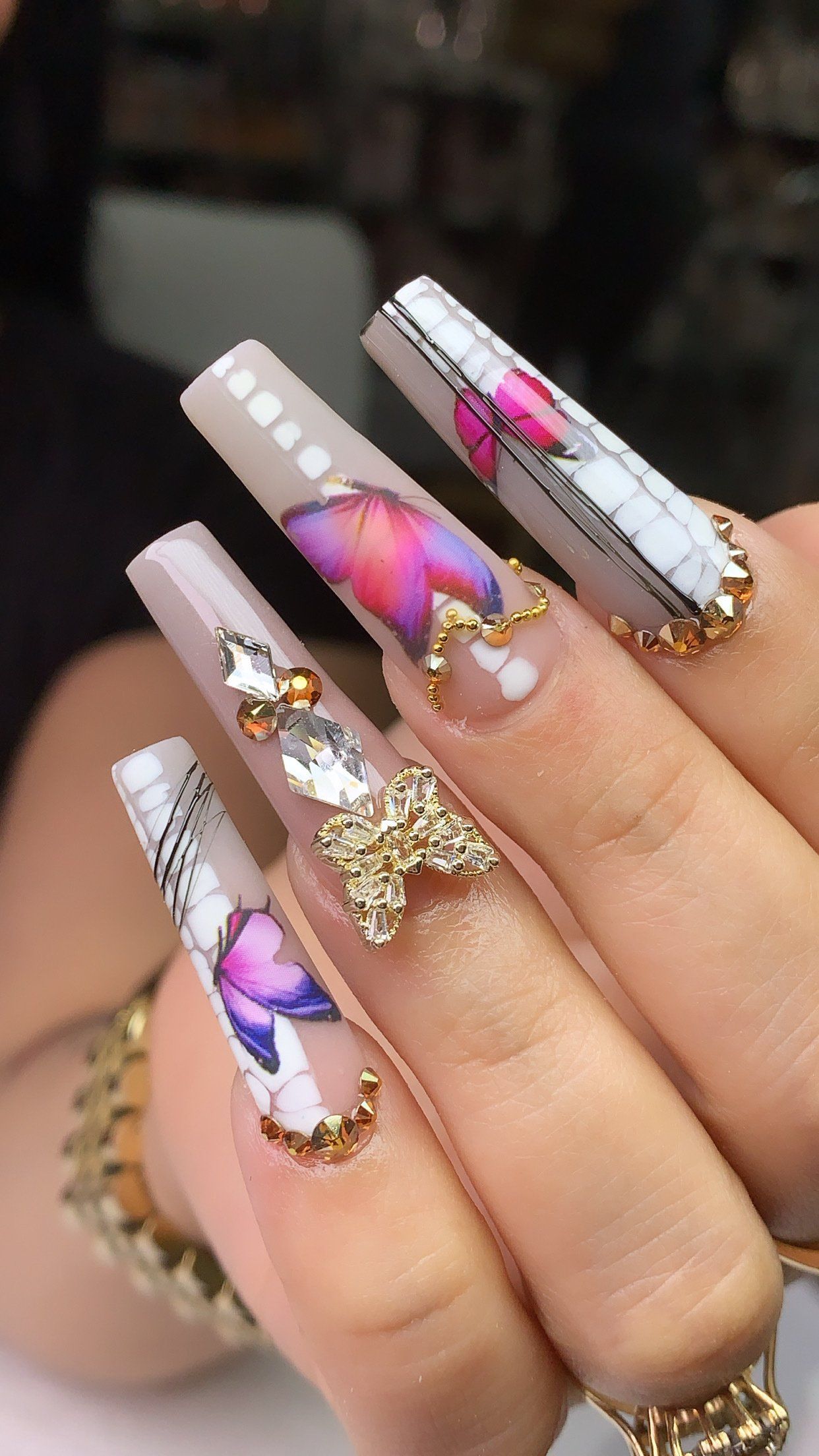 A woman 's nails are decorated with butterflies and rhinestones.