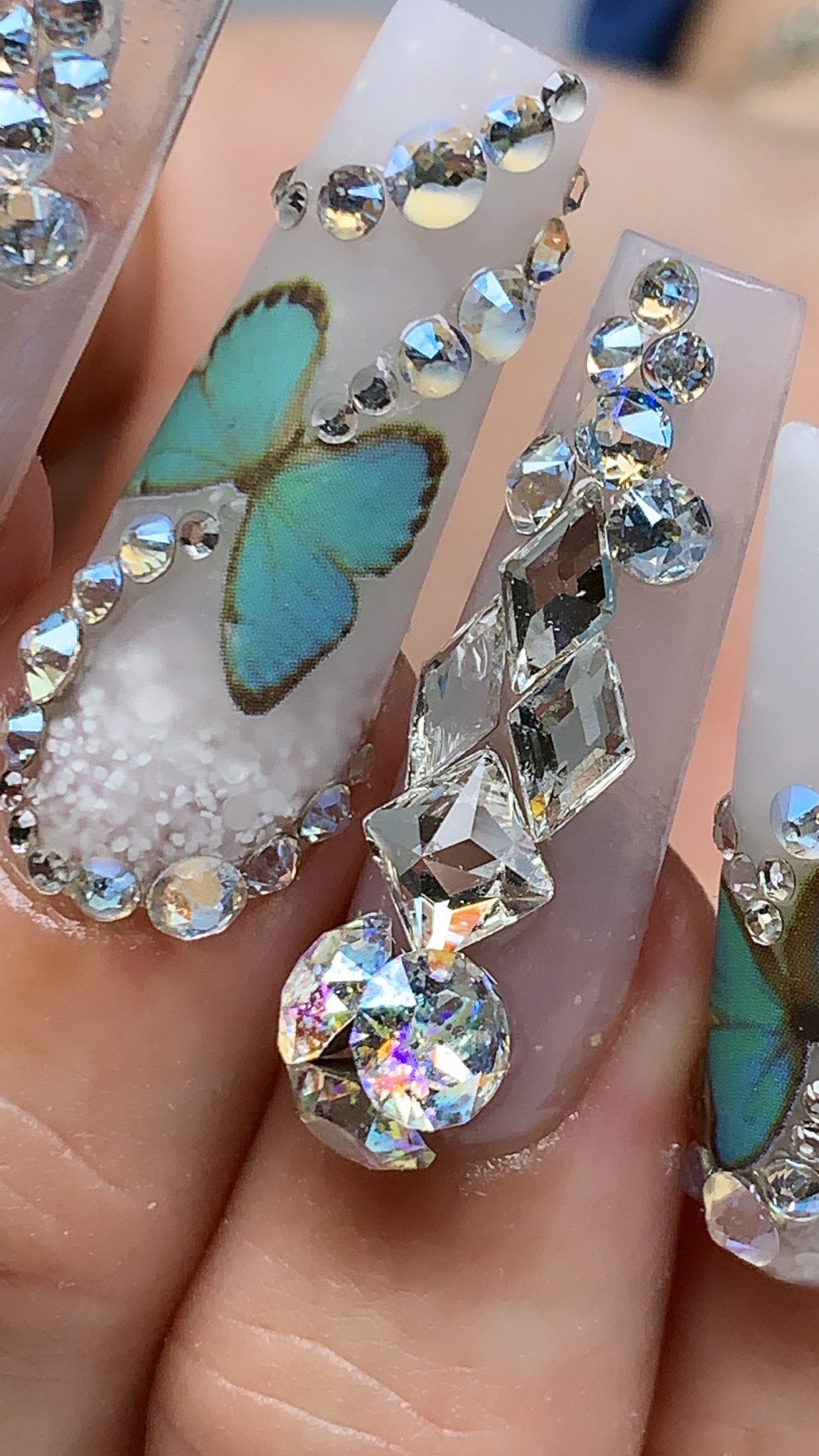 A close up of a person 's nails with a butterfly and rhinestones.