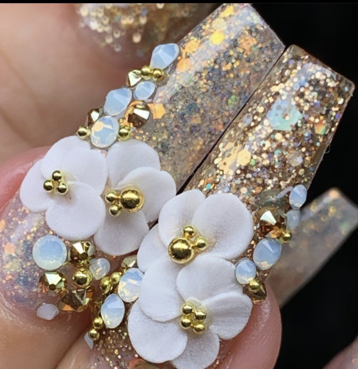 A woman 's nails are decorated with white flowers and gold glitter