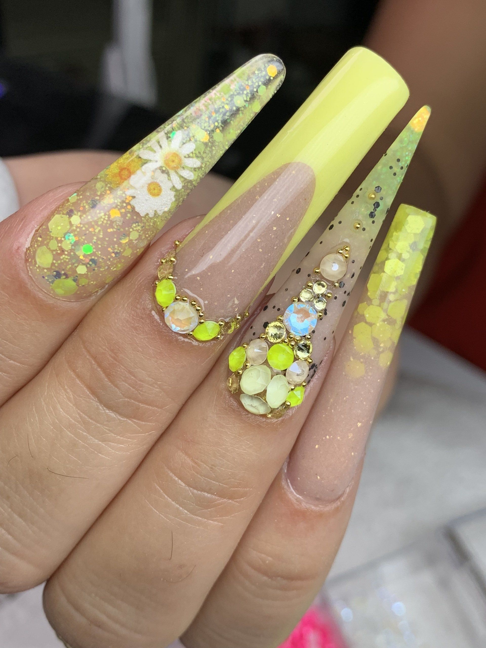 A close up of a person 's nails with yellow nails and rhinestones