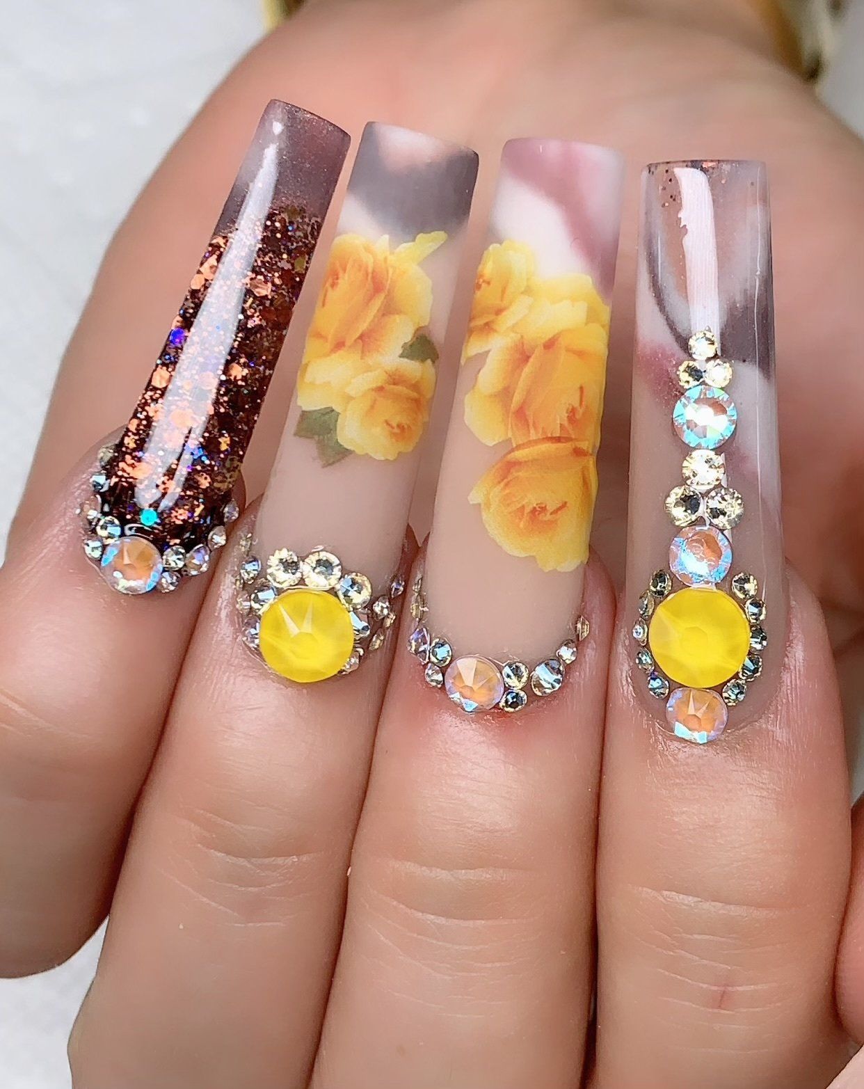 A close up of a woman 's nails with yellow flowers and rhinestones.