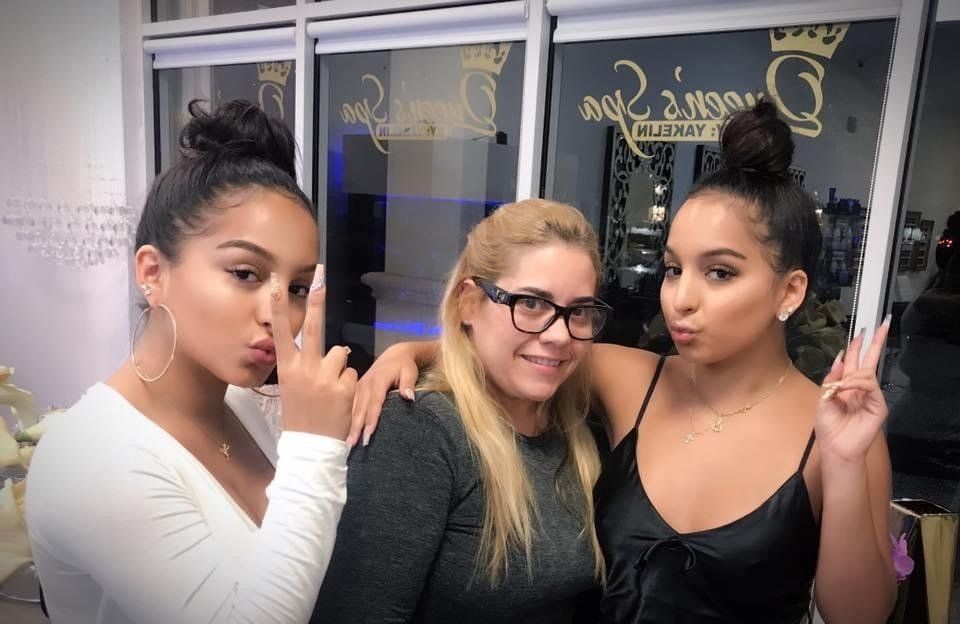 Three women are posing for a picture in front of a window.