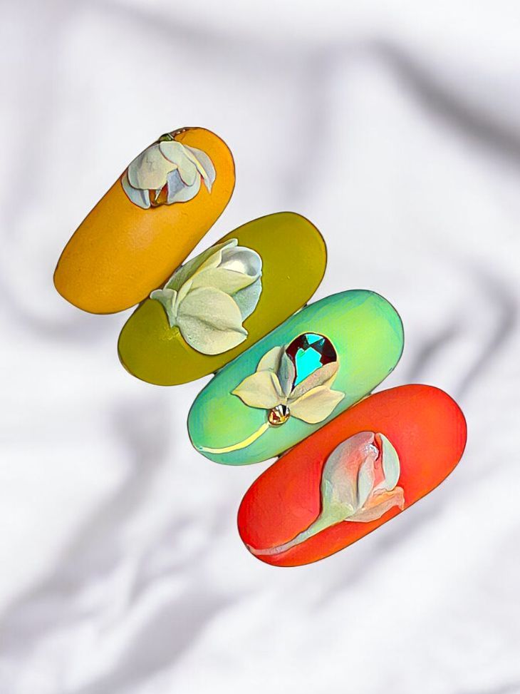 Three different colored nails with flowers on them on a white cloth.