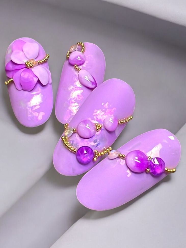 A close up of three purple nails with purple beads and flowers.