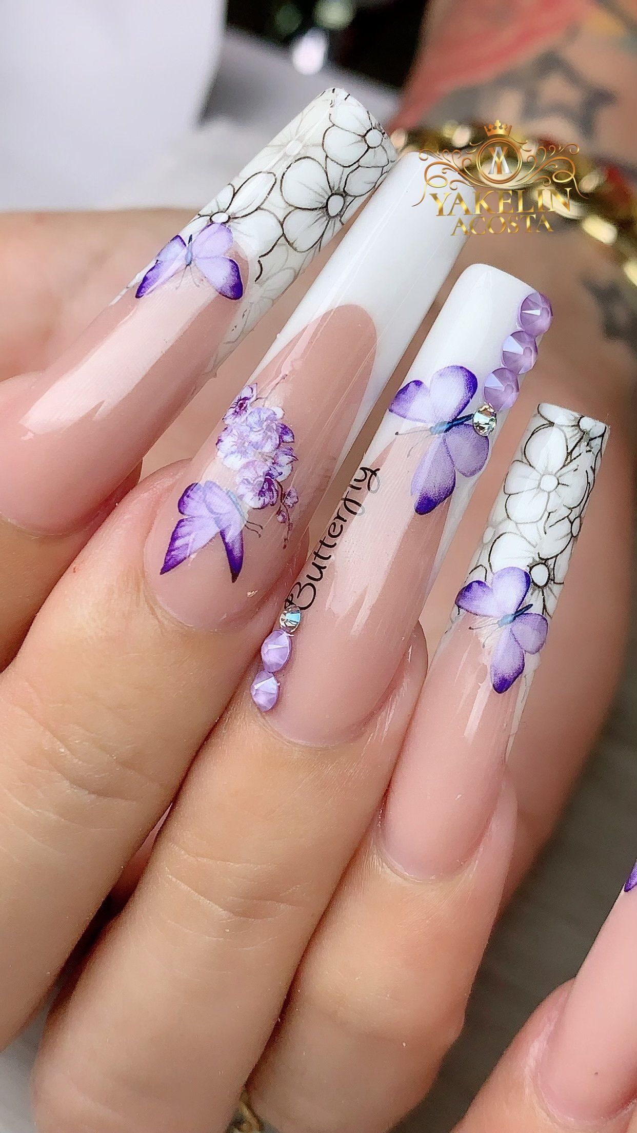 A close up of a person 's nails with purple butterflies and rhinestones.