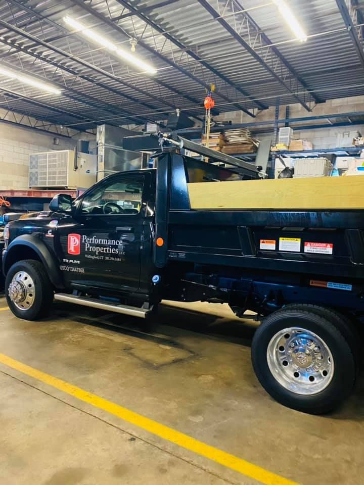 Black utility dump truck parked indoors in a warehouse garage, side view.
