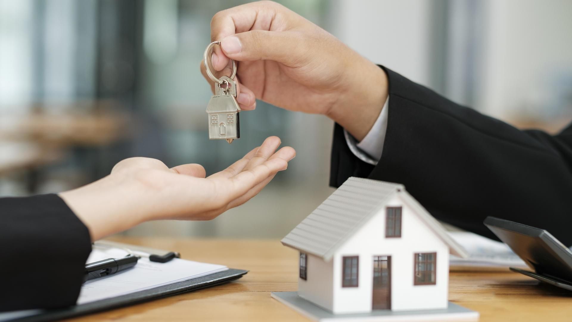 Handing over house keys during a real estate transaction beside a small model house