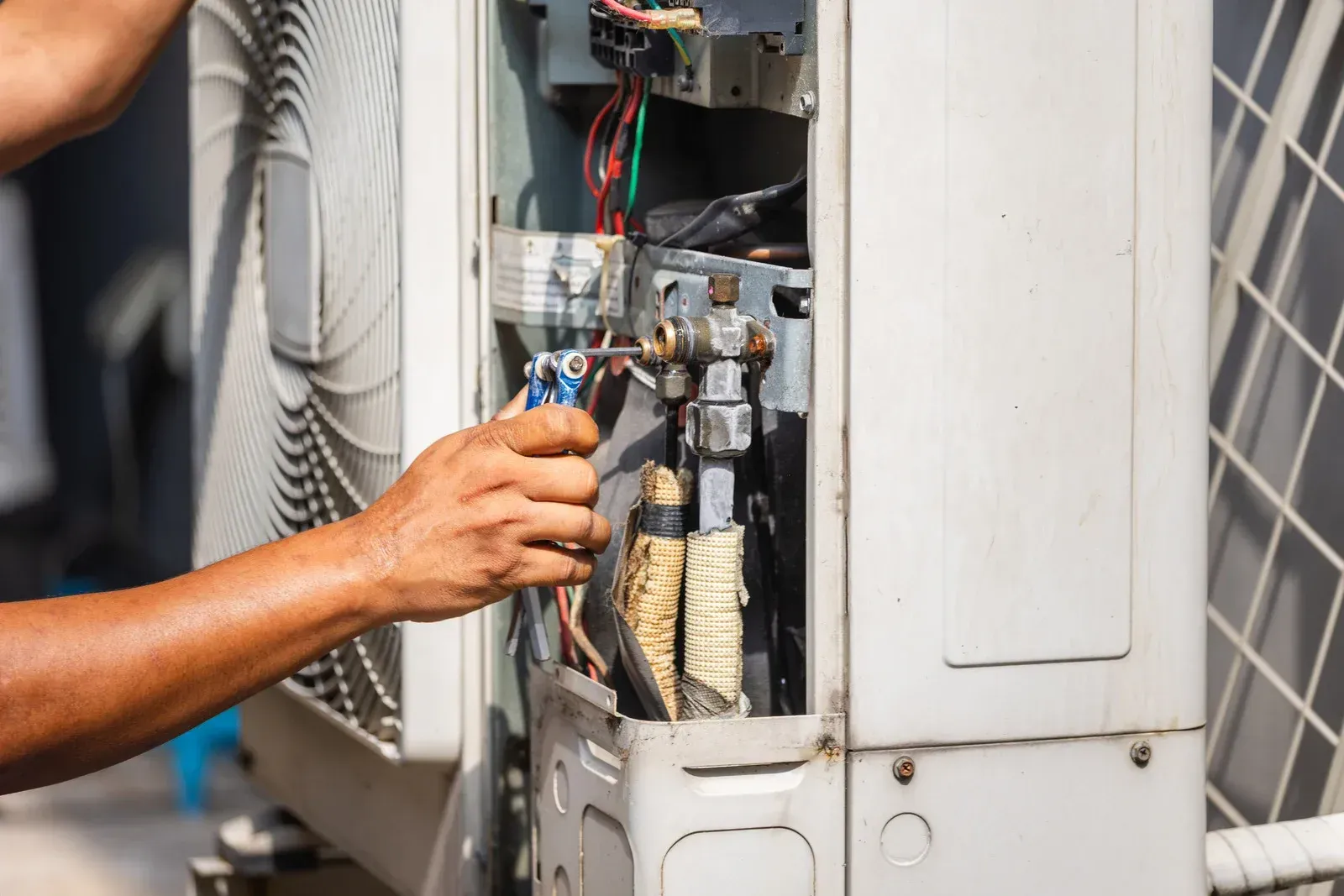 Technician repairing an outdoor HVAC unit with exposed wiring and components