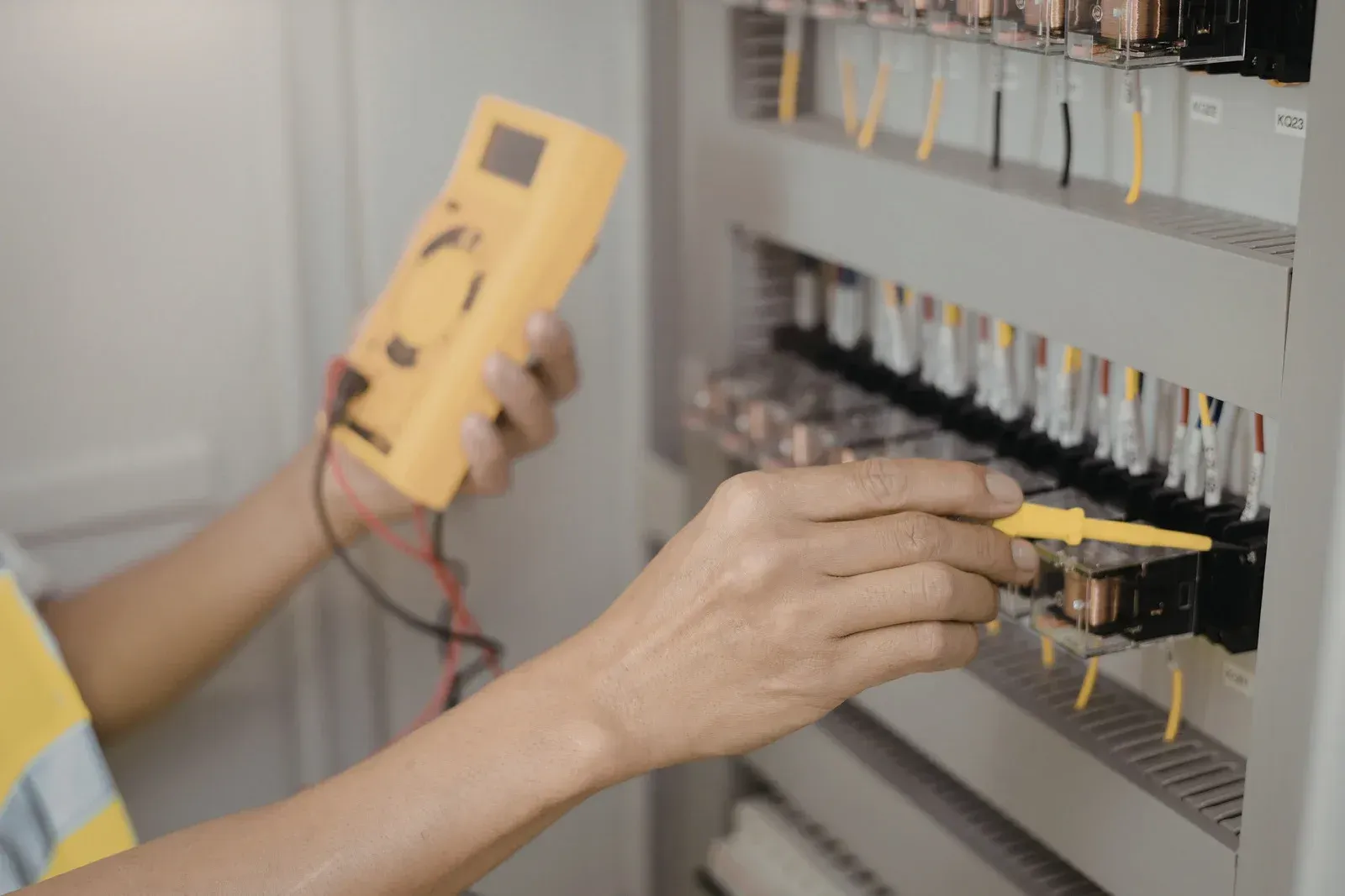 Technician testing an electrical panel with a yellow multimeter and hand tools