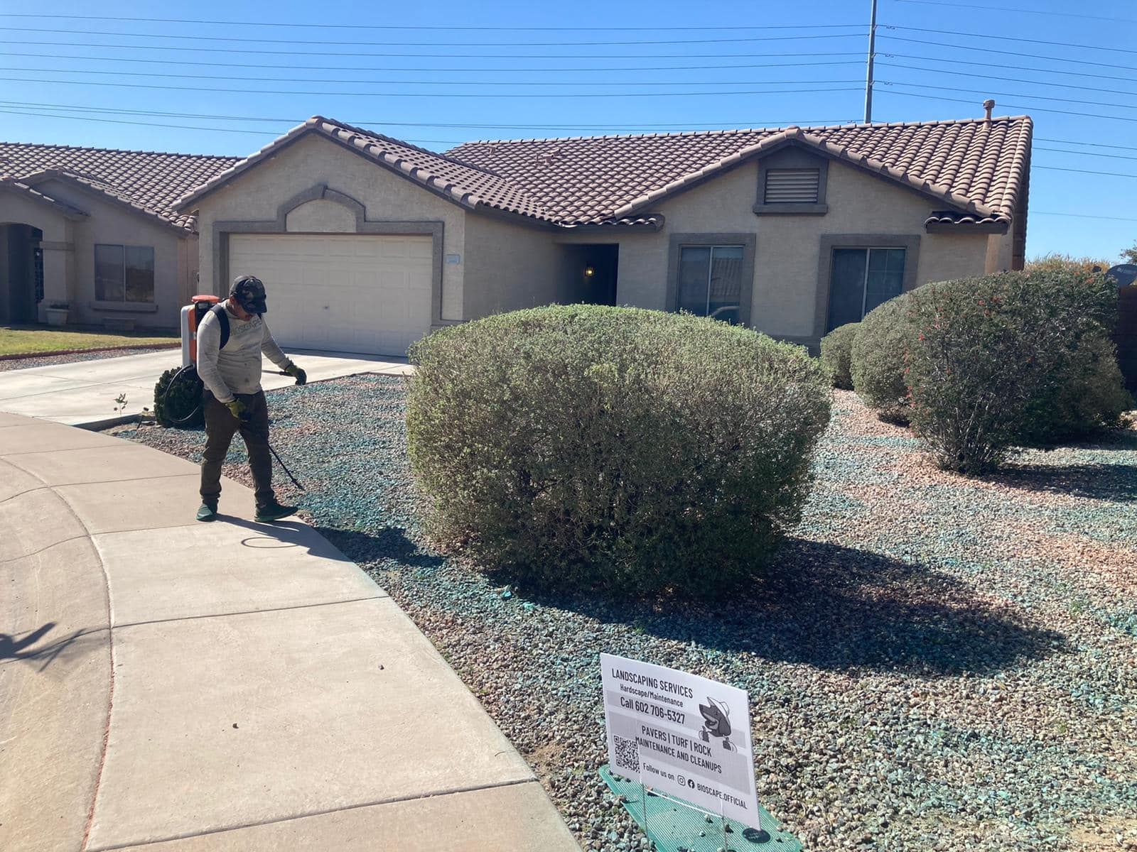 A man is standing in front of a house cutting bushes.