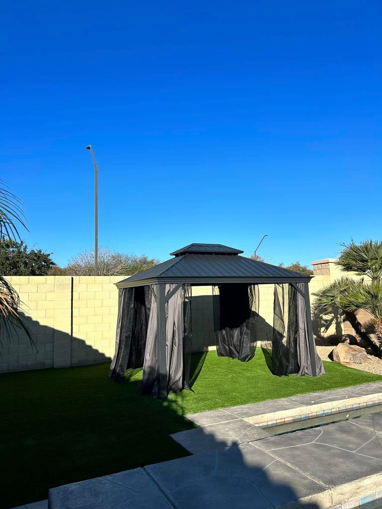 A gazebo is sitting in the middle of a lush green yard next to a swimming pool.
