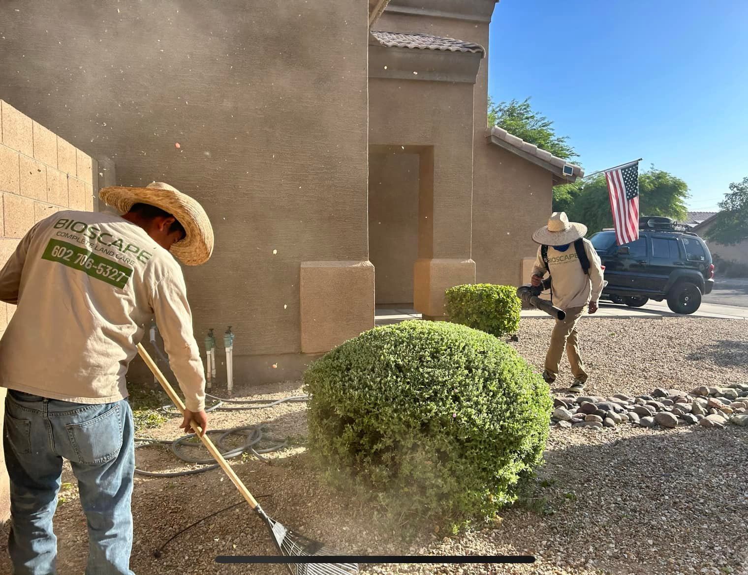 A man in a straw hat is raking a bush in front of a house.
