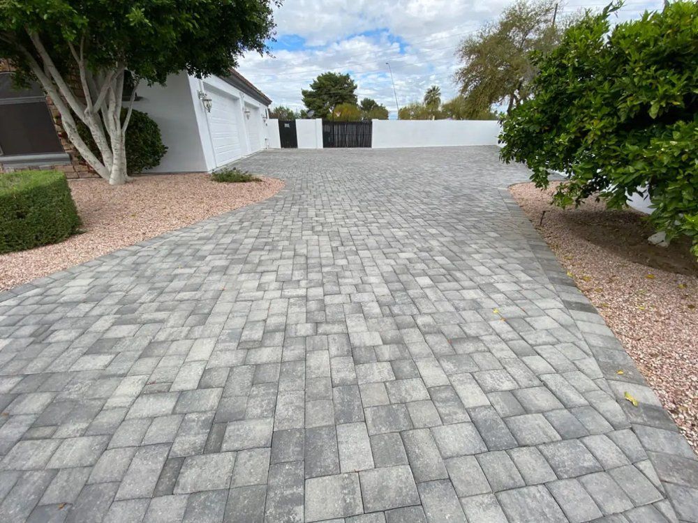 A brick driveway leading to a house with trees and bushes.