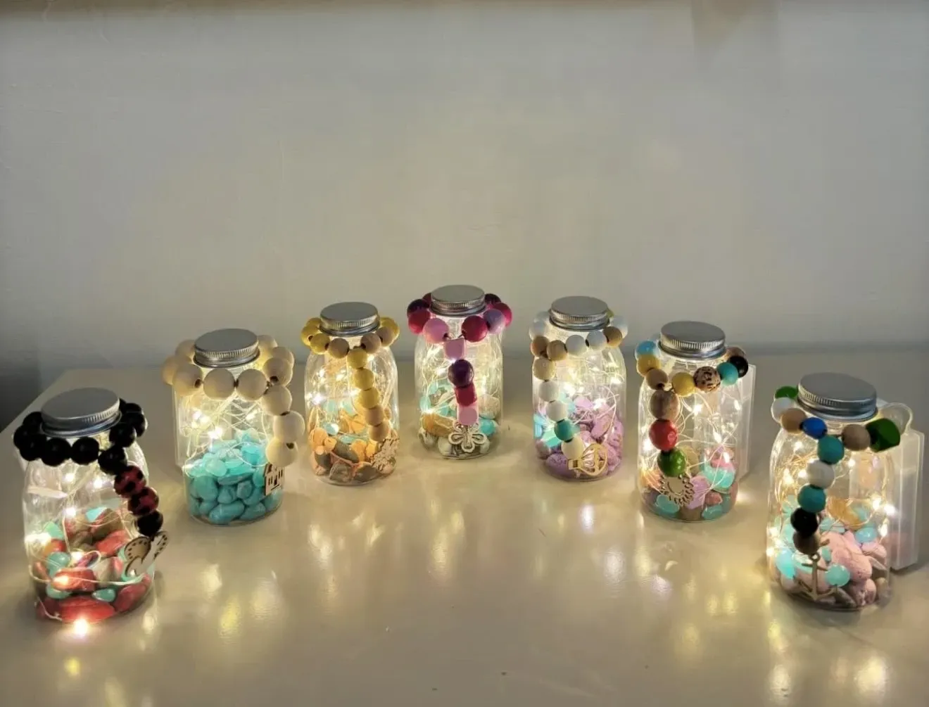 A group of jars filled with lights and beads are sitting on a table.