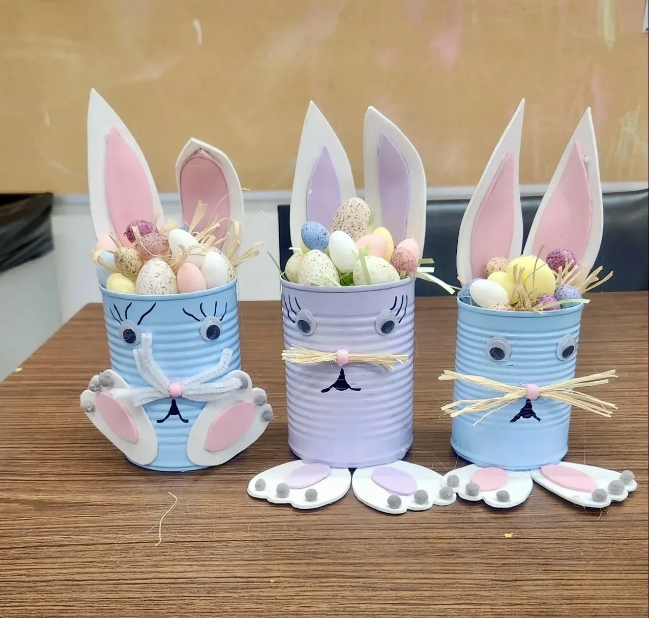 Three tin cans decorated to look like bunny rabbits filled with easter eggs.
