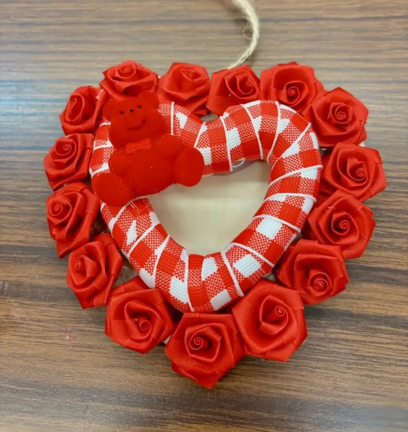 A heart shaped wreath with red roses and a teddy bear