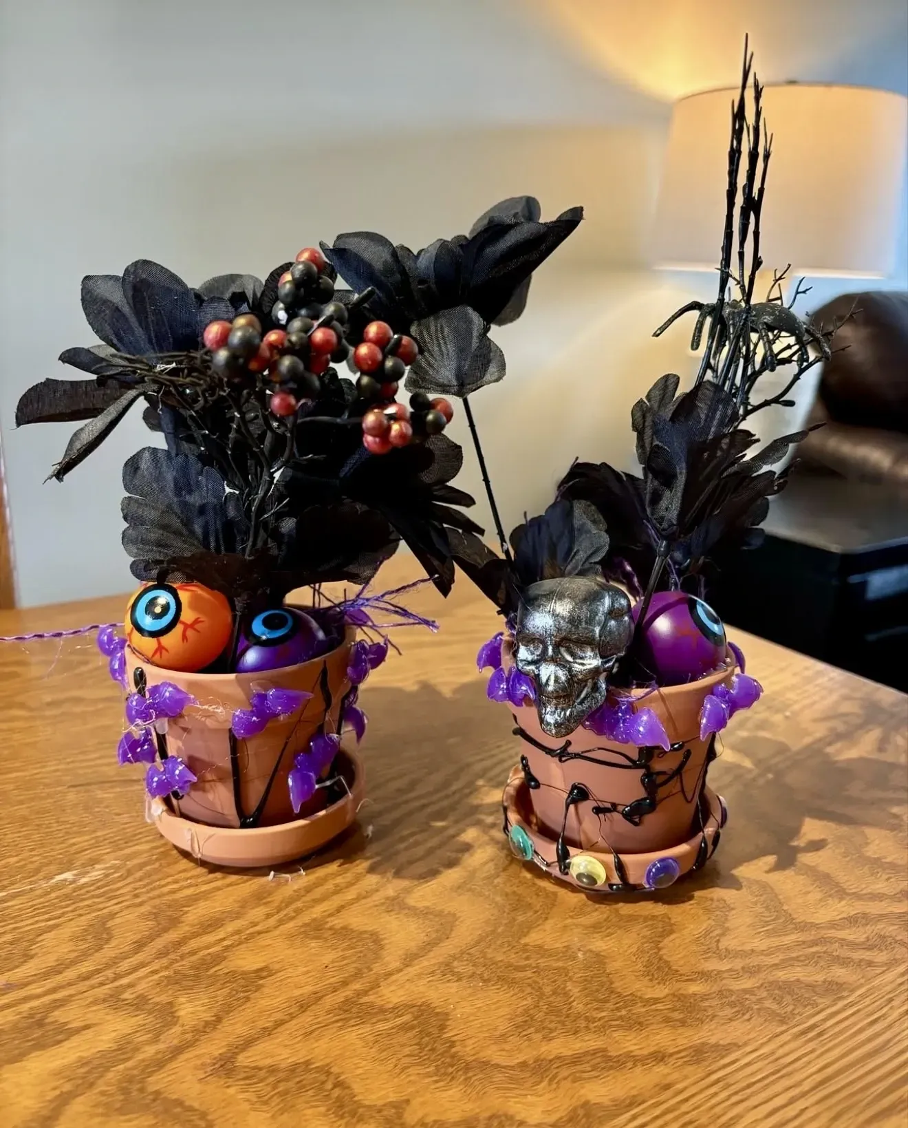 Two potted plants decorated for halloween are sitting on a wooden table.