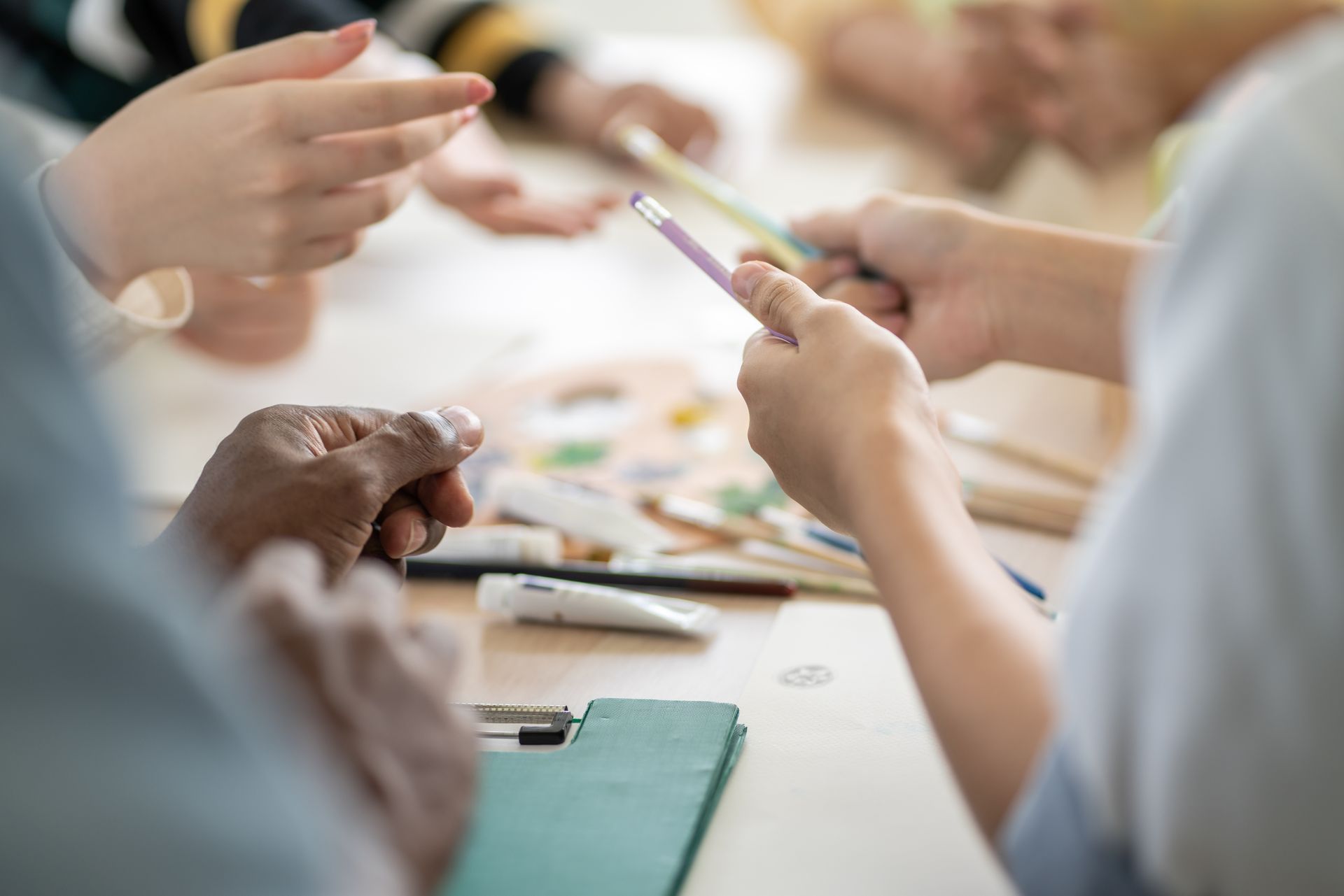 A group of people are sitting around a table holding pencils.