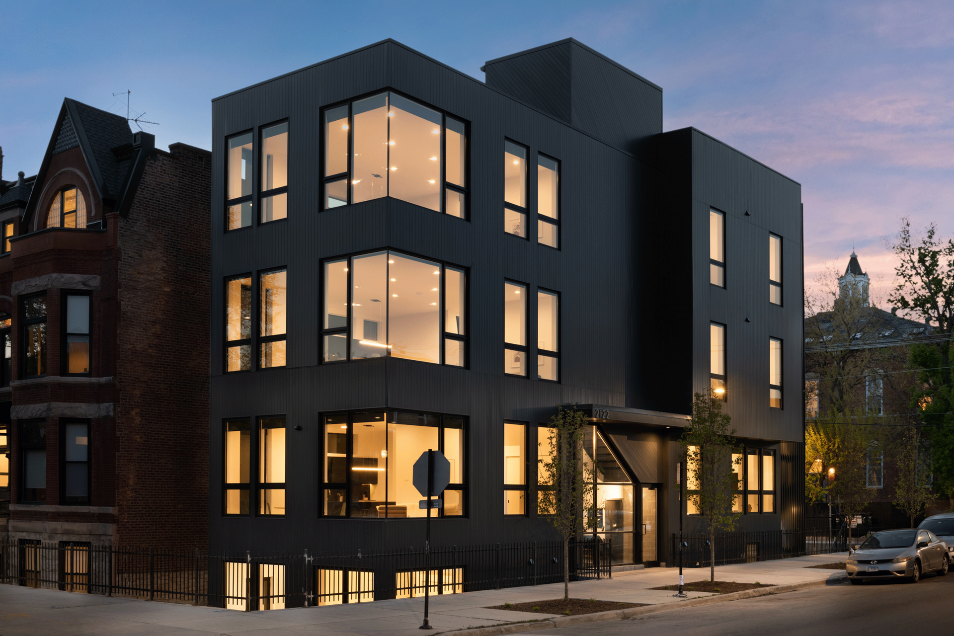 Modern, dark gray building with large windows, street view at dusk.