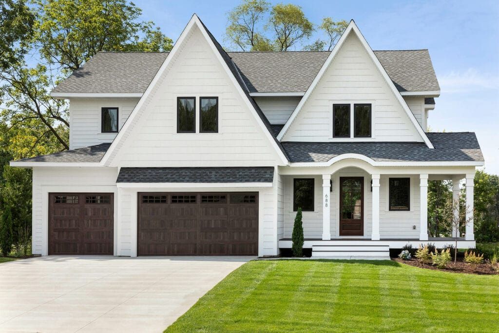 A large white house with two garage doors and a lush green lawn in front of it.